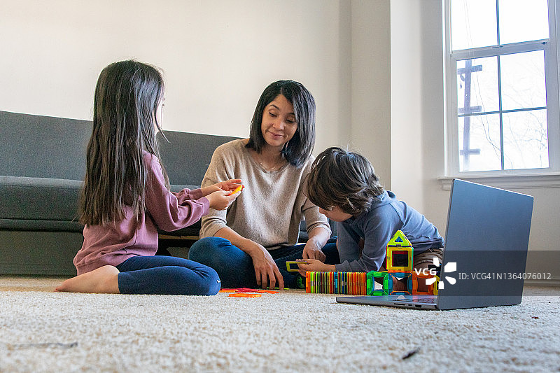 一位母亲和她的孩子们坐在客厅里玩笔记本电脑图片素材