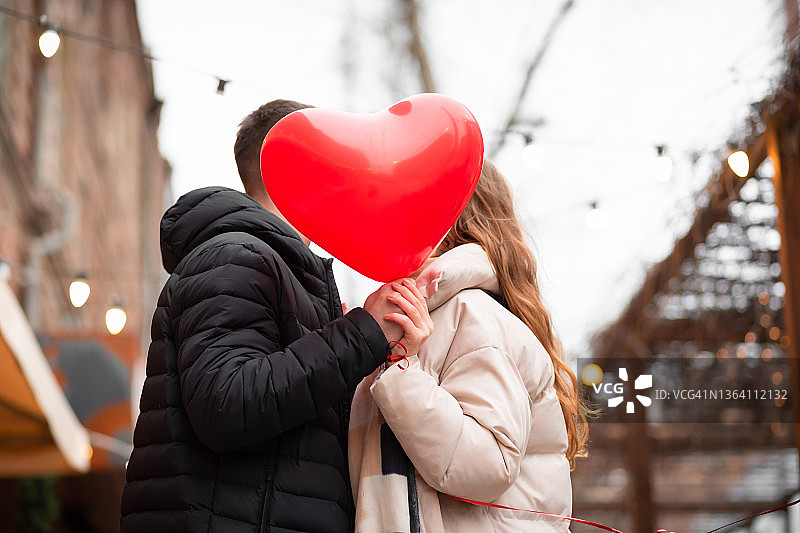一对情侣拿着心形气球在街上接吻。情人节概念，礼物，爱情图片素材
