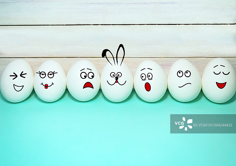 一排有着不同面部表情的彩蛋，以及一只以绿松石和木头为背景的复活节兔子。有趣的复活节彩蛋图片素材