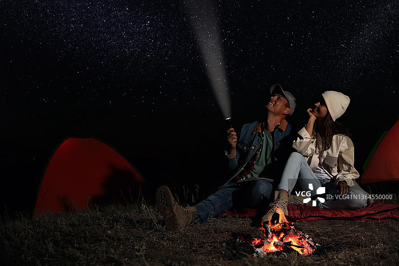 晚上拿着手电筒在篝火旁的幸福夫妻。露营的季节图片素材