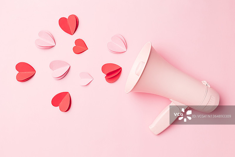 情人节背景扩音器和心形纸屑在粉红色的背景。图片素材