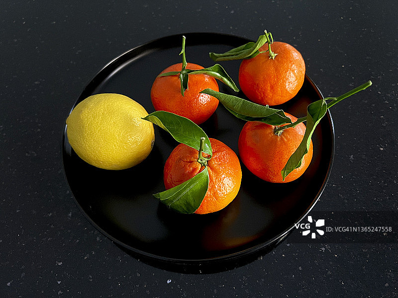 四个橘子和一个柠檬在黑色的盘子里，黑色的背景。图片素材