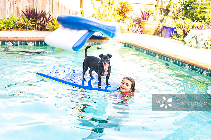 一只有趣的小狗和一个小女孩在后院的游泳池里冲浪图片素材