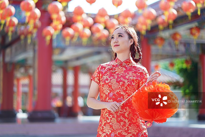 亚洲的中国妇女，穿着旗袍，举着中国灯笼。春节快乐图片素材