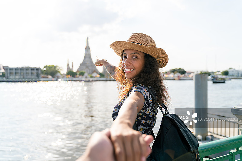 泰国曼谷，一名快乐的巴西女游客牵着男友的手，在湄南河和阿仑寺前享受旅行图片素材
