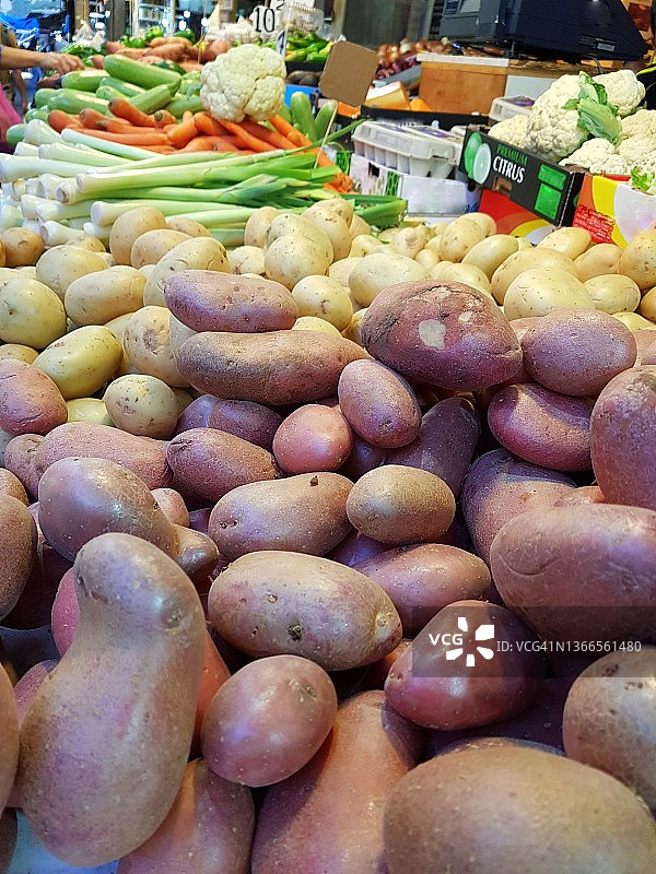 蔬菜市场摊位的特写，上面有粉色和黄色的土豆、韭菜、胡萝卜、西葫芦和卷心菜图片素材