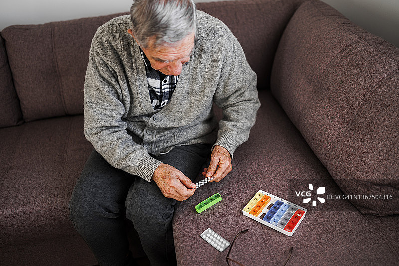 一名退休的老人将药丸从一个药瓶倒入他的手中，他将药物组织成一个每周药丸管理器。图片素材