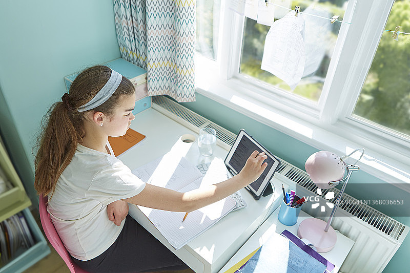 女孩在阳光明媚的卧室里用数码平板电脑在家学习图片素材