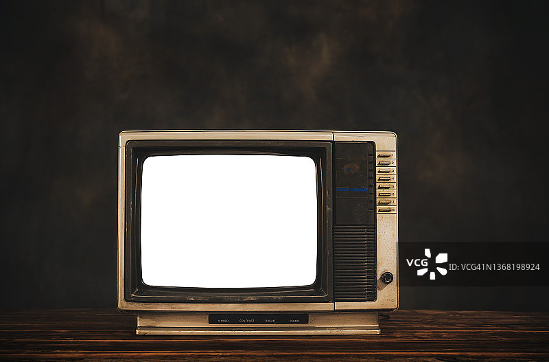 复古的老电视在木桌上与黑暗的墙壁背景，剪出白色的屏幕，静物电视图片素材