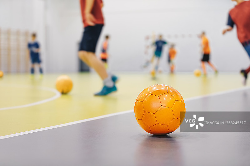室内训练场地的橙色五人制足球。年轻运动员在模糊背景下练习跑动球。学校儿童体育班图片素材