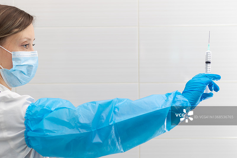 在冠状病毒大流行期间，医院中一名年轻女医生戴着医用口罩和手套，手里拿着注射器和听诊器。有选择性的重点图片素材