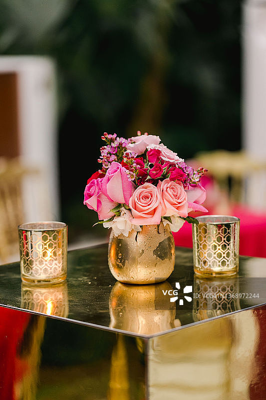 金色的花瓶放在金色的桌子上，装满了红色和粉色的玫瑰，这是婚礼彩排鸡尾酒会用的图片素材