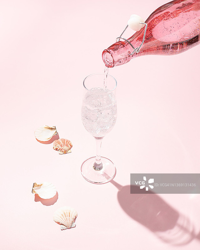 有创意的庆祝概念，由粉红色的瓶子在浅粉色的桌子上倒香槟酒和贝壳制成。艺术审美。图片素材