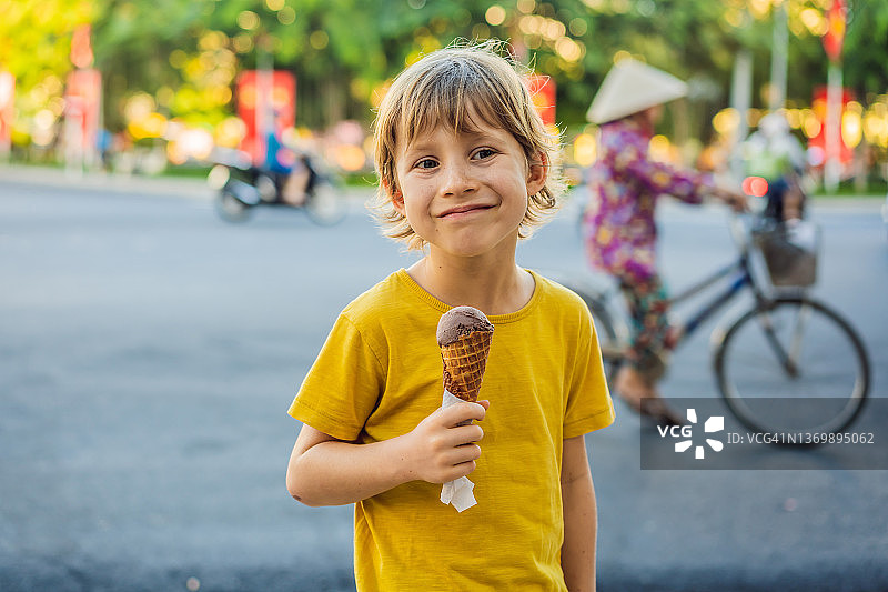 可爱的小男孩，在公园里吃着大冰激凌，对着镜头微笑，夏天图片素材