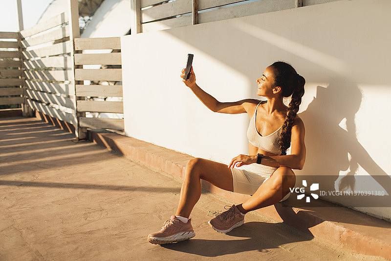 年轻迷人的运动女性微笑着，在户外锻炼后用智能手机自拍图片素材