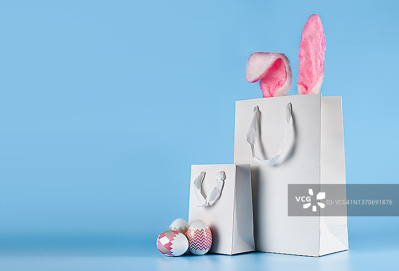 蓝色背景的横幅。网上购物的概念为复活节，采购和销售的假期。带有兔子耳朵和复活节彩蛋的礼物袋图片素材