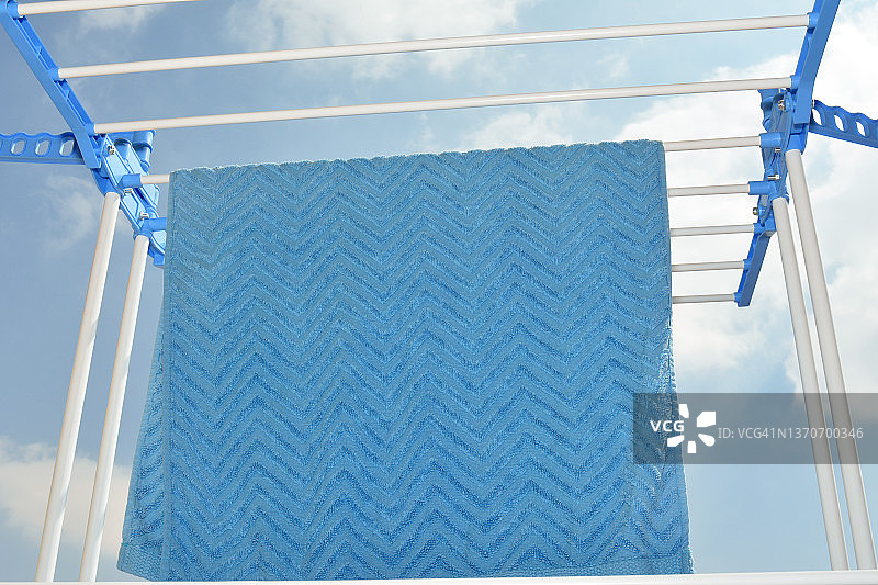 一条蓝色的棉面巾放在塑料多层晾衣架上晾晒，衬着蓝色多云的天空，洗衣、作业和卫生概念图片素材
