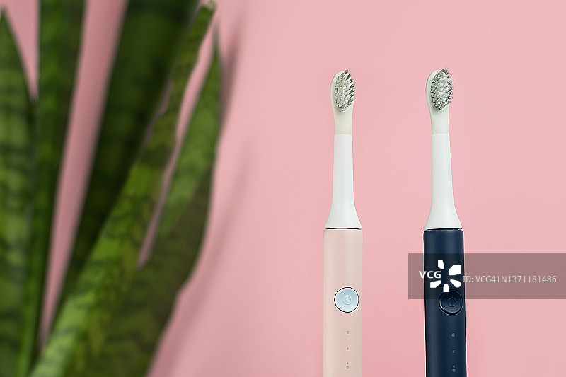新型现代超声波牙刷。牙齿护理用品与绿色的叶子粉红色的粉彩背景。口腔卫生，牙龈健康，牙齿健康。牙科产品超声波振动牙刷图片素材