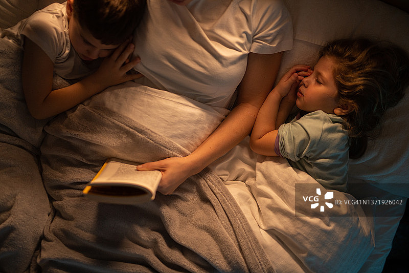 孩子们躺在床上睡觉时，母亲给他们讲故事，然后才说悄悄话图片素材