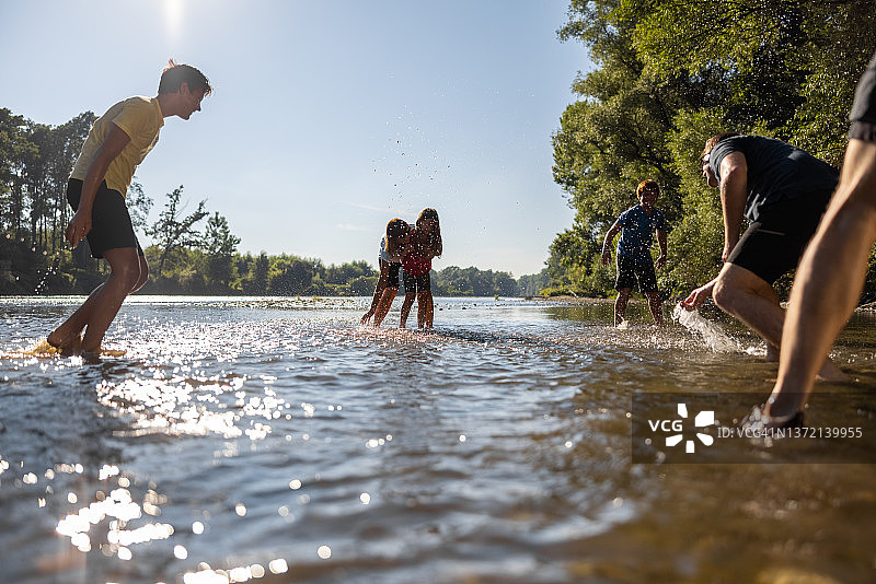 父母们站在河床上，和孩子们在河里玩耍，用水打湿对方图片素材