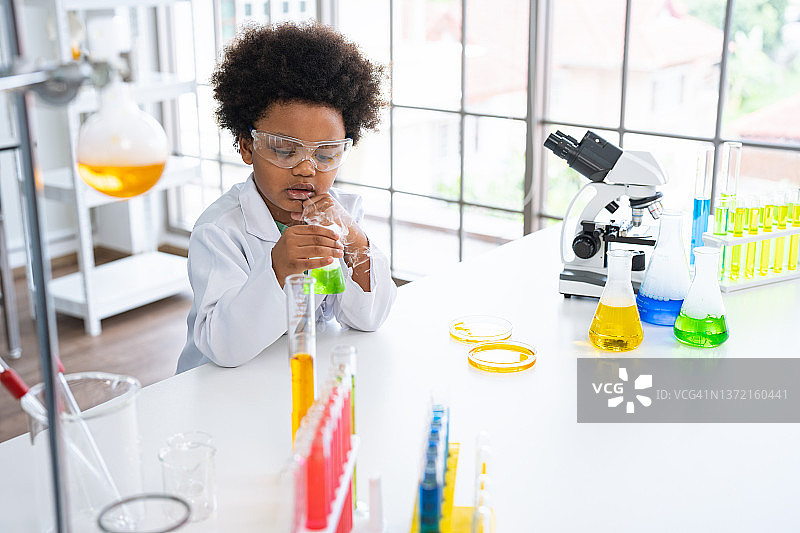 非洲裔美国可爱的小男孩学生在科学课上学习研究和做化学实验，同时在玻璃杯中分析和混合液体图片素材
