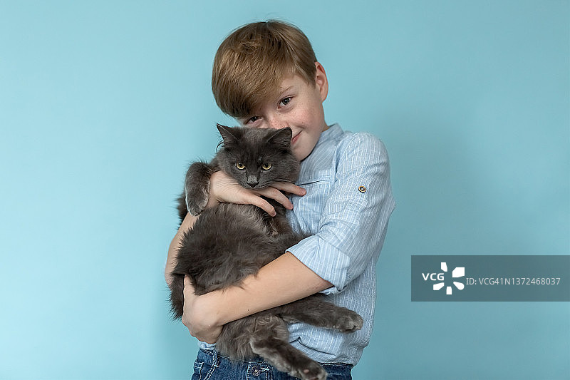 一个漂亮的金发男孩怀里抱着一只灰色的猫。图片素材