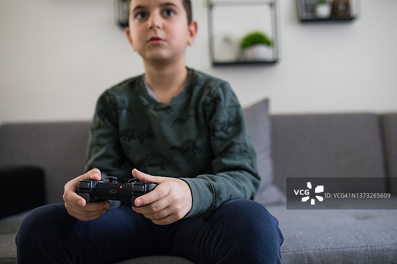 男孩坐在家里的沙发上玩电子游戏图片素材
