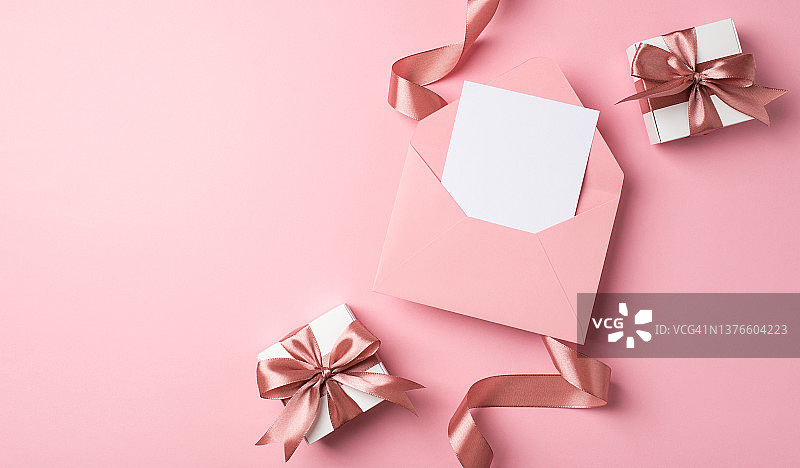 顶视图照片的情人节装饰两个白色礼品盒粉红色蝴蝶结卷曲的丝带和打开粉红色信封与纸表在孤立的粉彩粉红色背景与空白空间图片素材