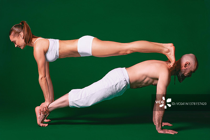 美丽的运动女人和男人在白色的衣服做瑜伽体式在室内绿色的背景图片素材