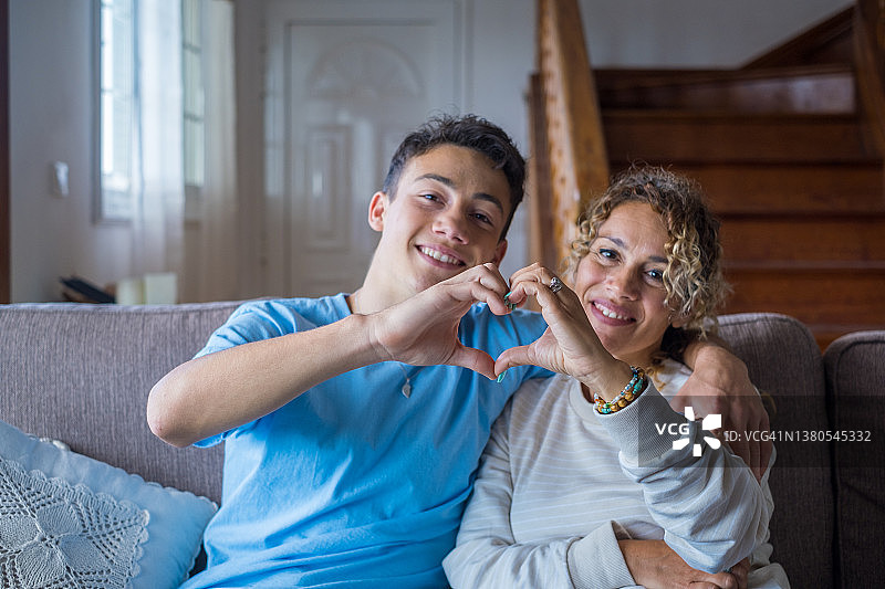 一对母亲和儿子在一起的家庭的肖像，用他们的手指和手与脸在背景制作一个爱心形状。深情的少年和女人享受图片素材