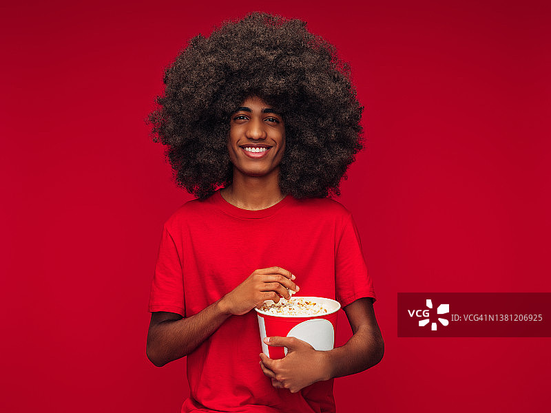 美丽的非洲发型男子吃爆米花孤立的红色背景图片素材