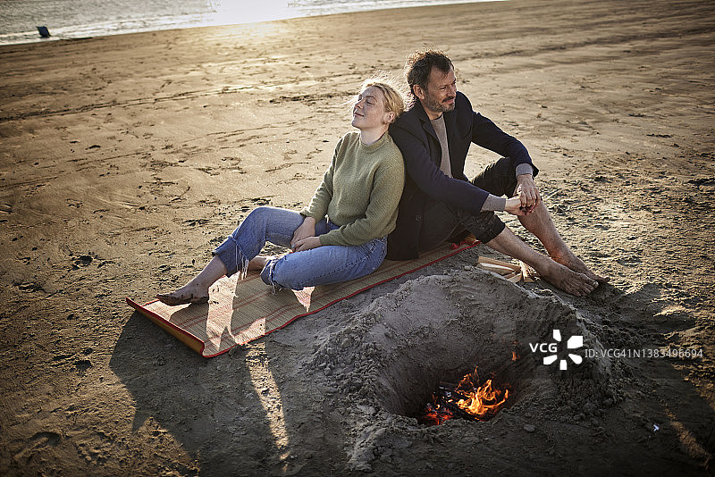 父亲和已成年的女儿坐在沙滩上的营火旁图片素材