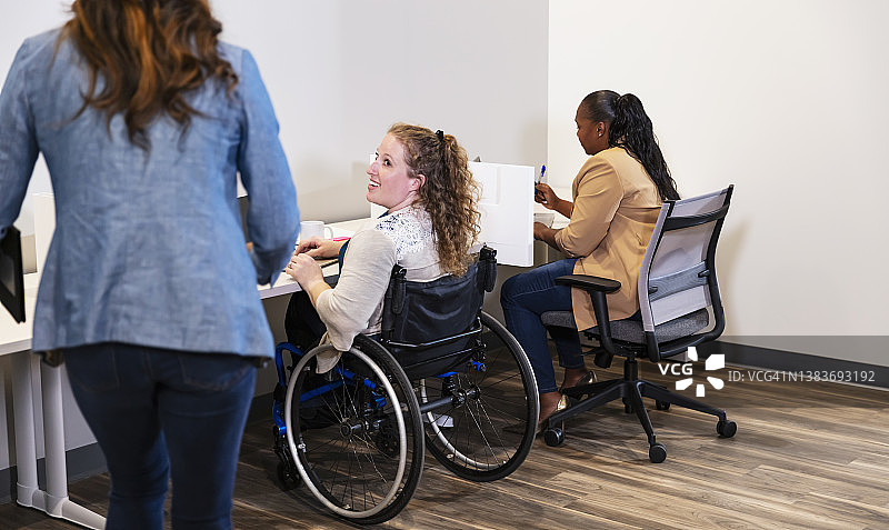 坐在轮椅上工作的女士和同事打招呼图片素材
