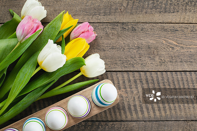 春天郁金香的花束和木制背景上的手工彩色复活节彩蛋。春天的节日。俯视图，平躺图片素材
