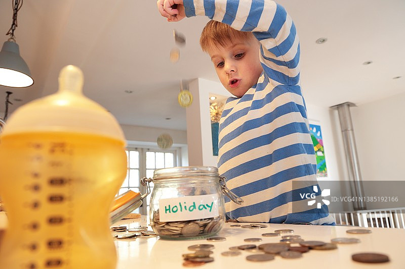 小男孩在玻璃罐里存钱图片素材