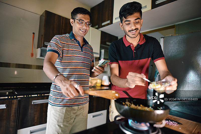 一个中年男子和一个十几岁的男孩在厨房里一起烹饪食谱图片素材