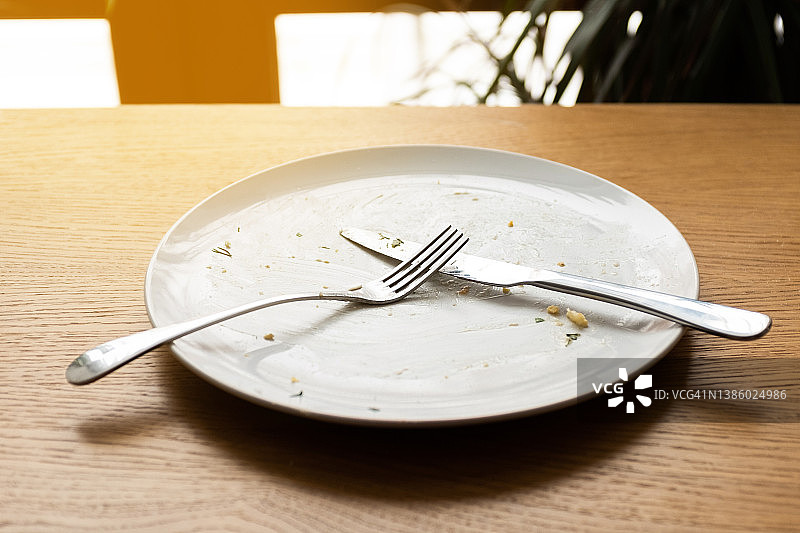 木桌上有一个又脏又空的盘子和刀叉。象征午餐或晚餐结束的餐具。图片素材