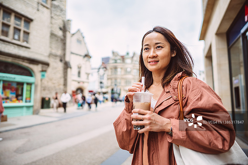 年轻的女游客一边享受着冰饮料一边走在市中心的大街上图片素材