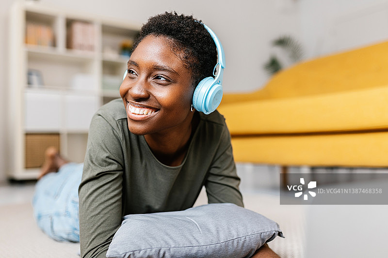 快乐的年轻非洲裔美国妇女戴着耳机听音乐，而放松在家里图片素材