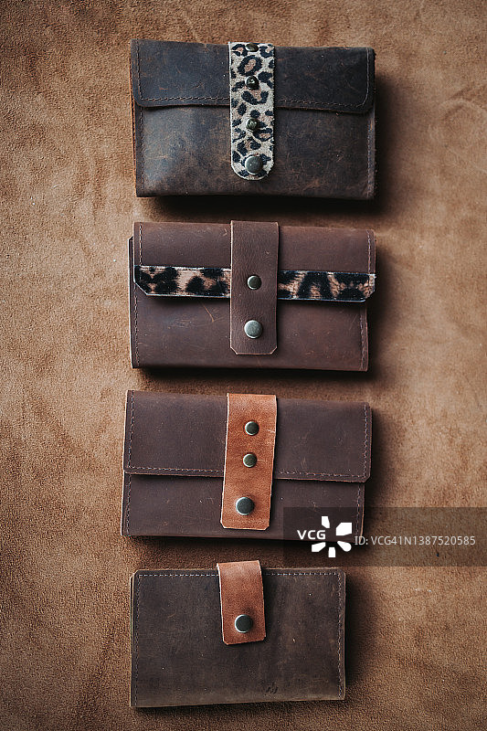 四个成品皮革钱包在一个棕色皮革床单。图片素材