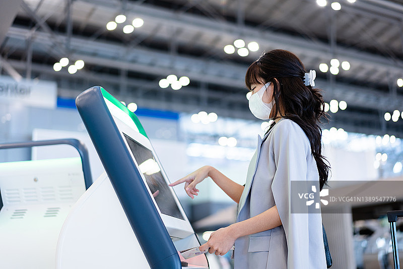 戴着防护口罩的亚洲年轻女商人在机场的机器上做自我检查图片素材