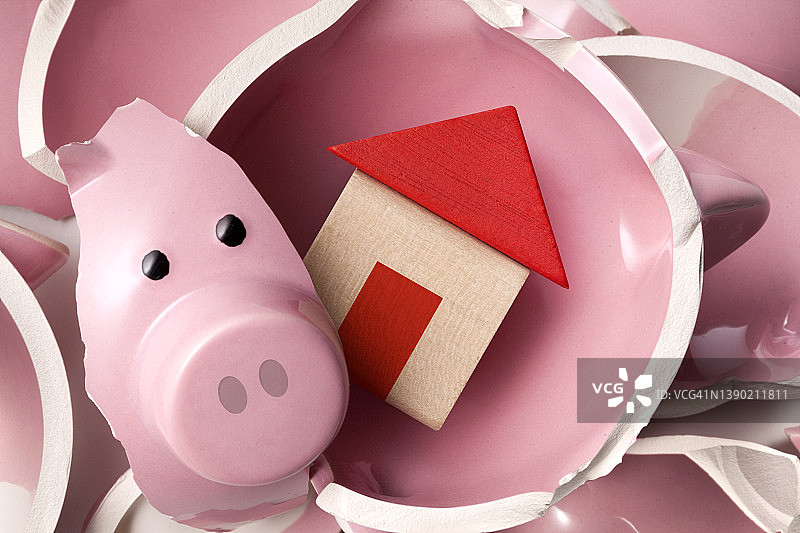 存钱买房子。坏了的小猪存钱罐和迷你房子模型。图片素材