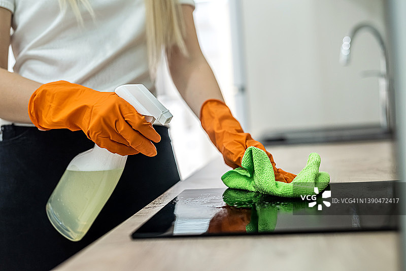 戴着橙色手套的漂亮女人用手擦拭厨房表面的灰尘图片素材