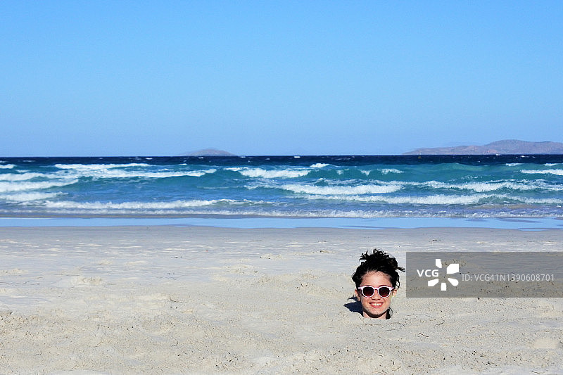 小女孩在海滩上把头埋在沙子里图片素材