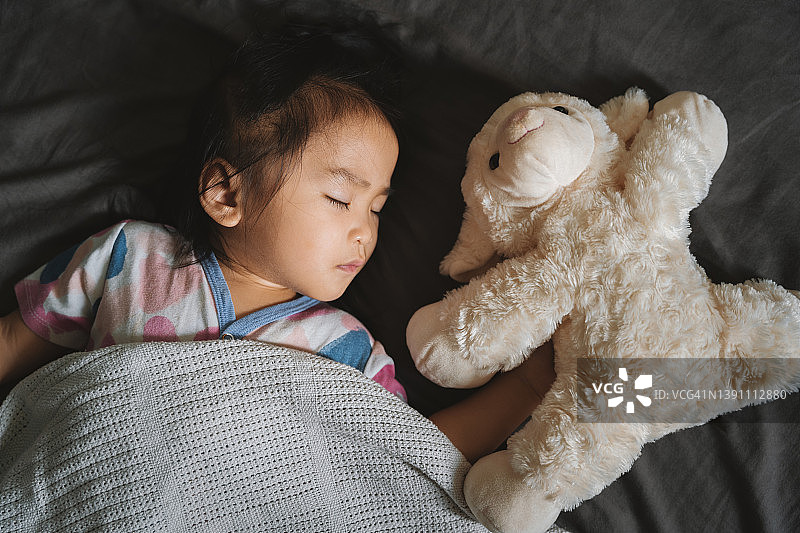 蹒跚学步的小女孩抱着她的毛绒玩具睡在床上图片素材