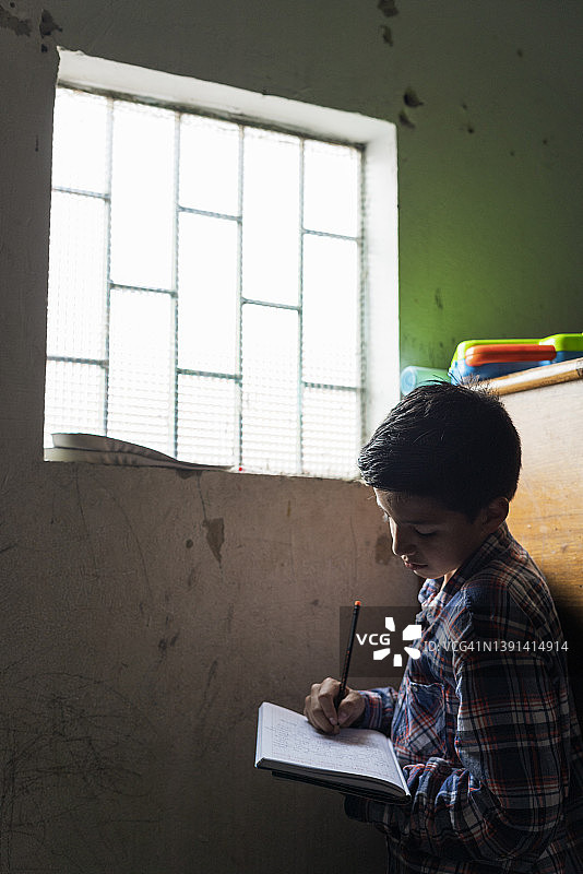 一个低收入的西班牙裔男孩，平均年龄11岁，正坐在房间里做作业图片素材