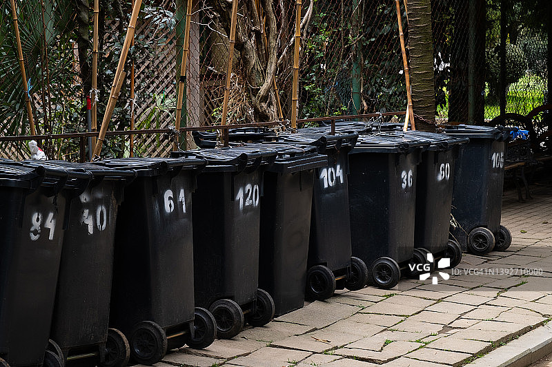 黑色塑料垃圾桶或垃圾箱，有轮子的坦克，用于移动和运输，站在街上。环保理念，可持续生活方式。回收的垃圾。图片素材