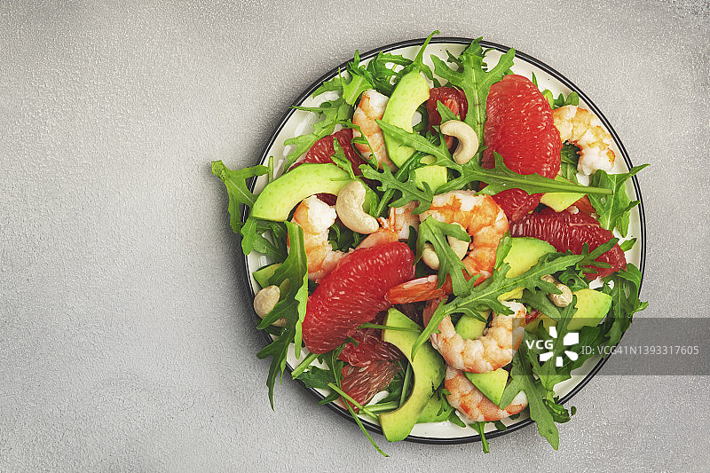 美味的沙拉，有虾，鳄梨，葡萄柚，芝麻菜和腰果。灰色石桌背景，俯视图，负空间图片素材
