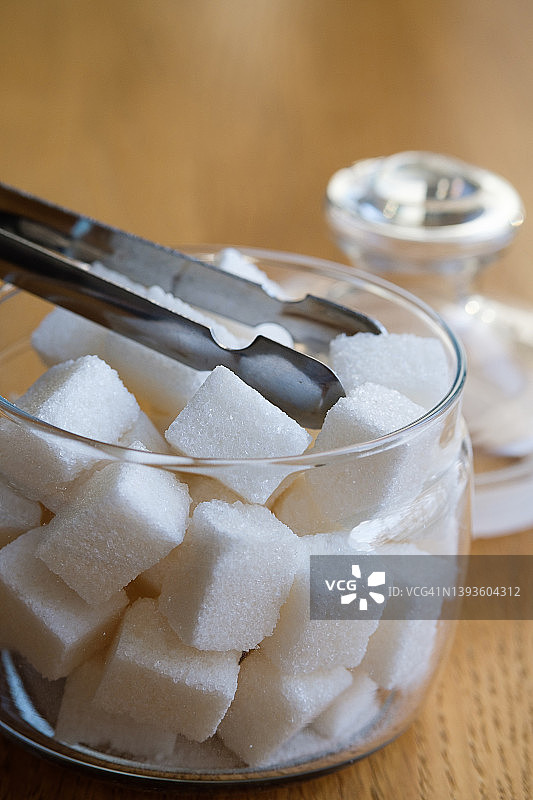 在家里，在咖啡馆，自助餐厅或餐馆里，把方糖放在透明的玻璃糖碗里，放在木桌或背景上。营养不良和生活方式的概念。图片素材