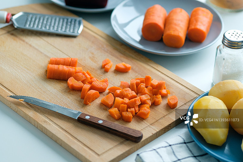 煮熟的胡萝卜,切成小方块。准备一种蔬菜沙拉，叫做油醋酱。菜刀放在菜板上切蔬菜。附近还有其他食材。素食和纯素食品的概念。图片素材
